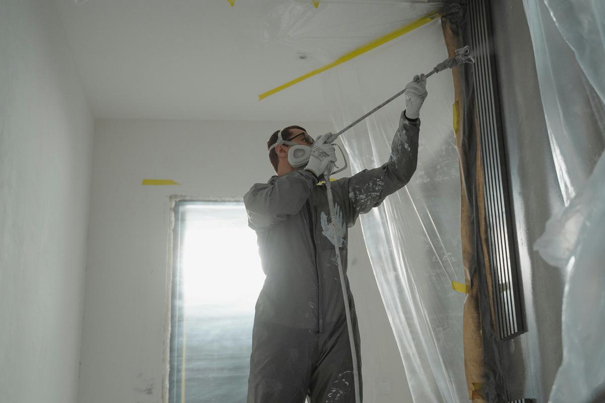 Worker in a respirator and protective suit beside plastic sheeting over a work area (sample photo)