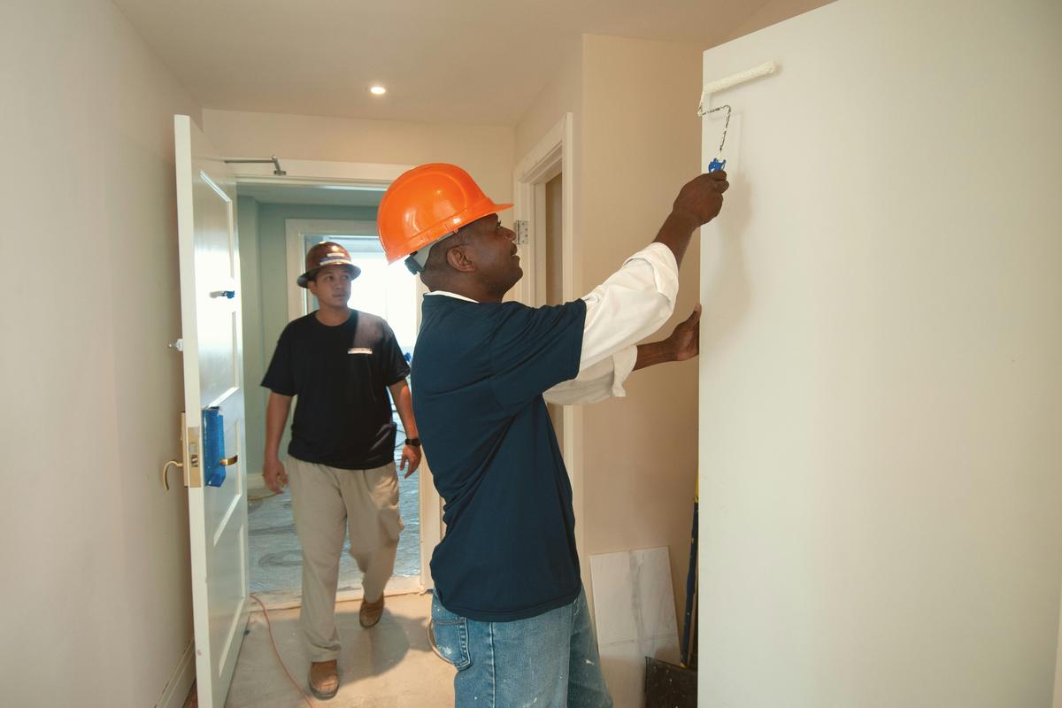 Two workers in a hallway, one in a hard hat checking a door frame (sample photo)